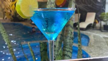 Cóctel azul con un adorno de lima en una copa de martini, sobre una superficie reflectante.