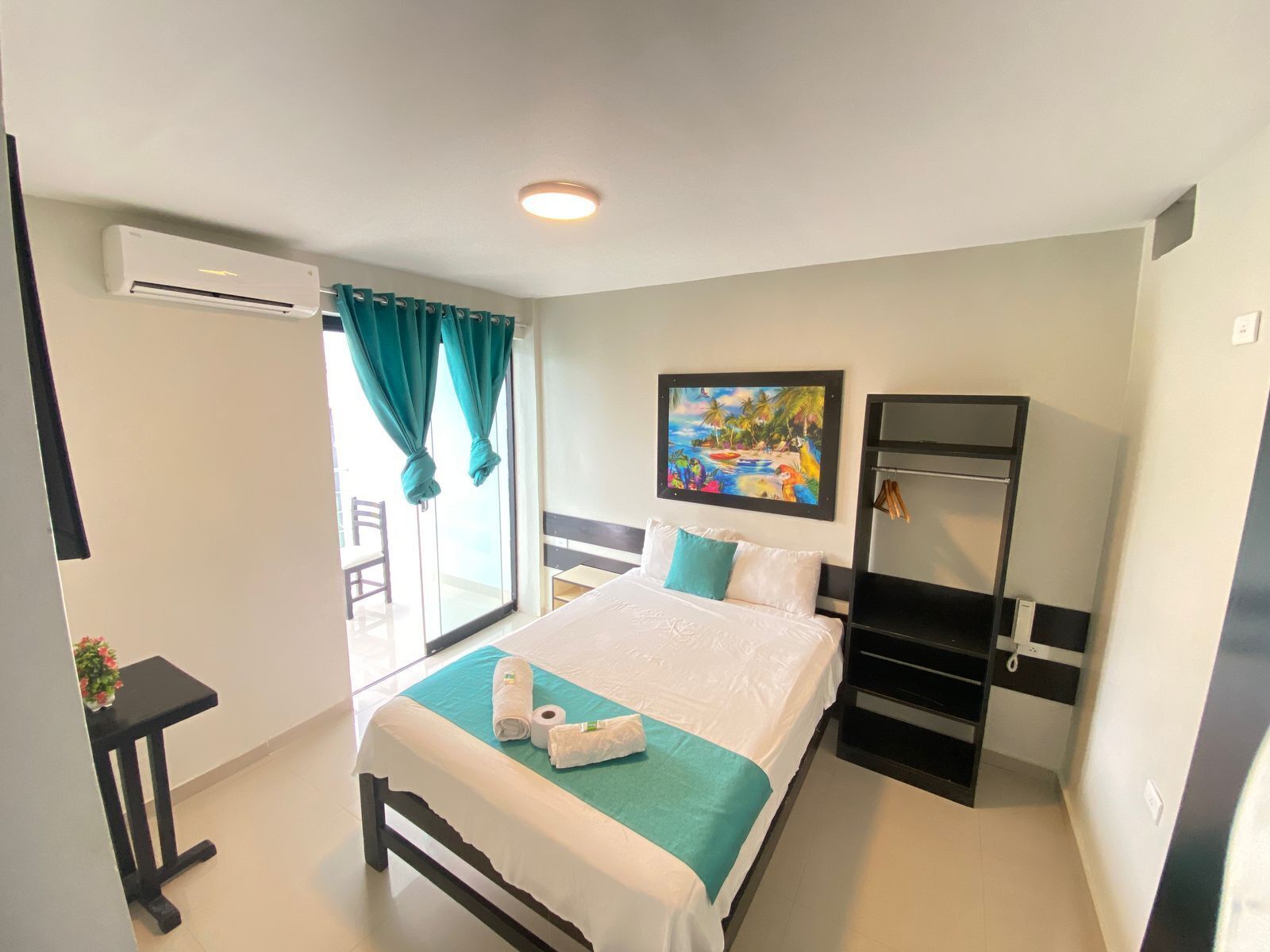 A hotel room with a bed, a painting, a wardrobe, and a window with curtains.
