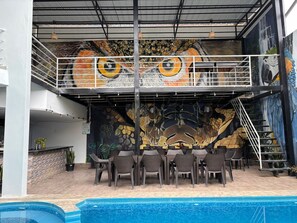 A poolside area with a mural of a large eye, outdoor seating, and a staircase. - HOTEL COSTA AZUL (La Banda de Shilcayo)