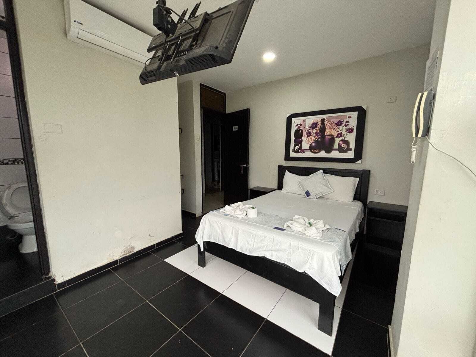 A hotel room with a bed, a painting on the wall, and a ceiling fan.
