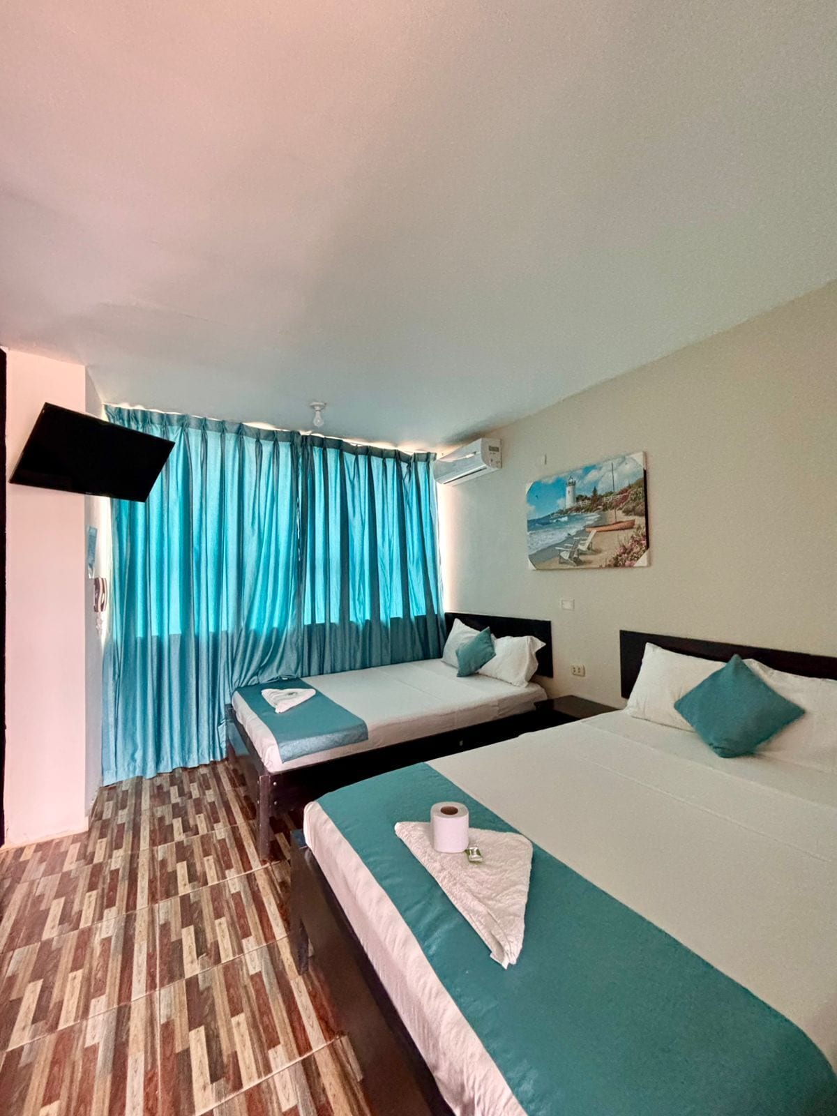 A hotel room with two beds, a flat-screen TV, a painting on the wall, and a patterned floor.