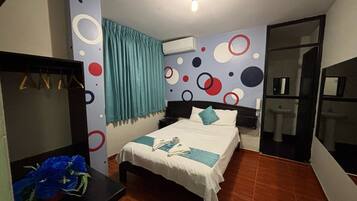 Habitación de hotel con cama, escritorio, espejo, armario, baño con lavamanos e inodoro, y una pared con diseños circulares.