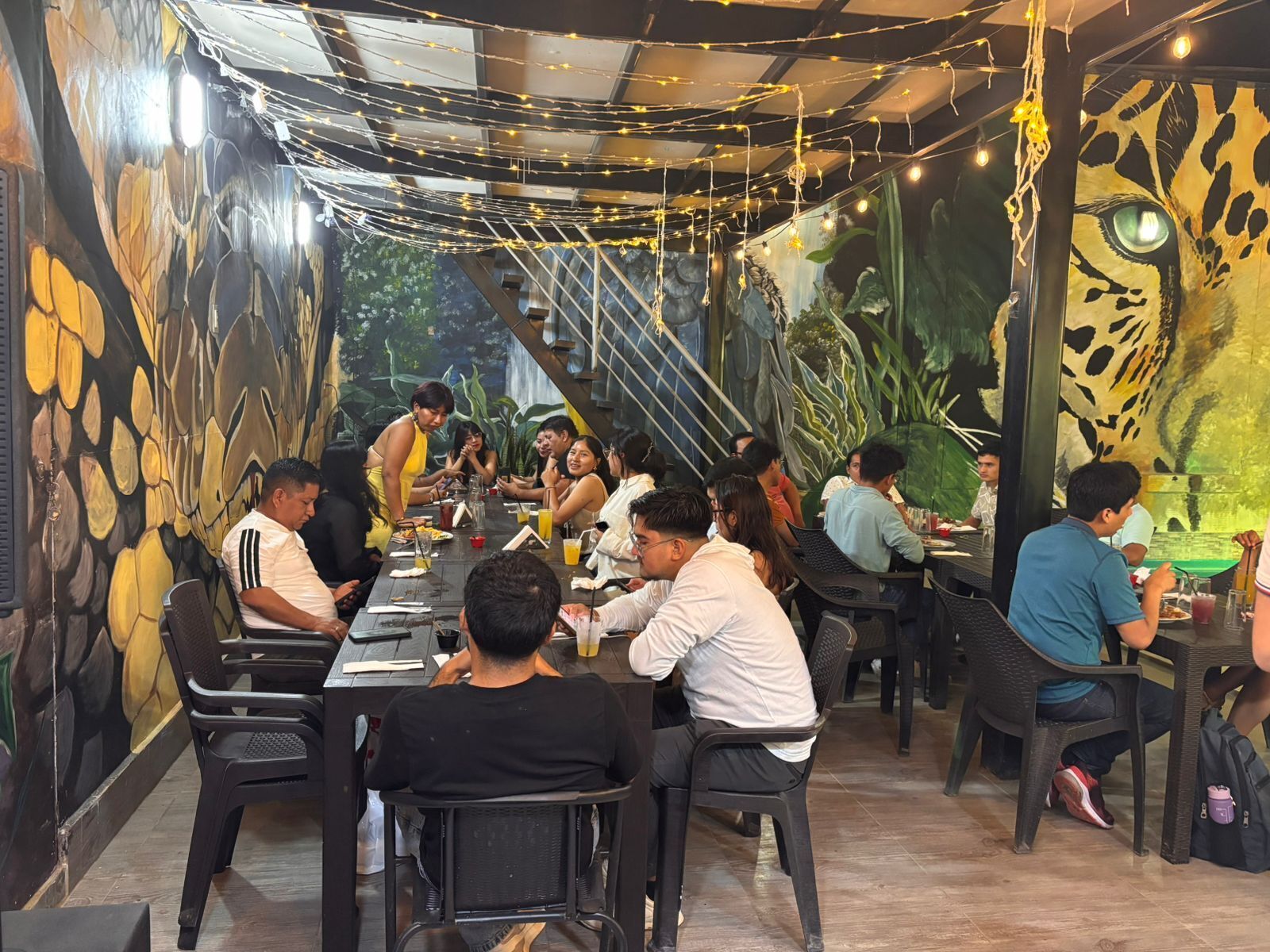 An indoor dining area with tables and chairs, a mural on the wall, and string lights.