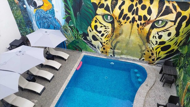 A swimming pool with lounge chairs and umbrellas, surrounded by a mural of a leopard. - HOTEL COSTA AZUL (La Banda de Shilcayo)