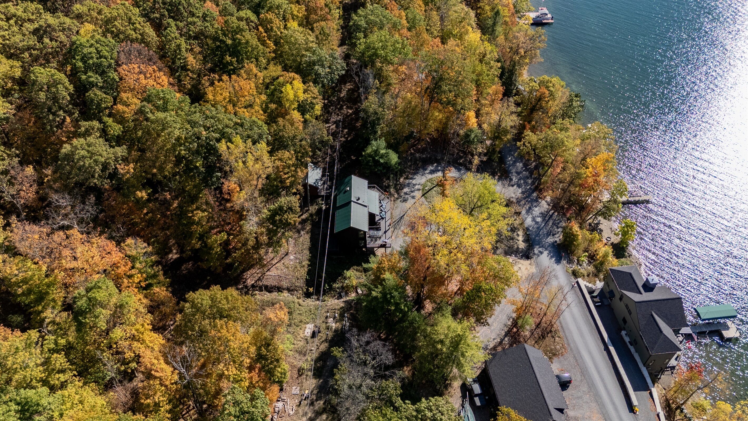 An aerial view of a cabin surrounded by dense forest with a lake in the background.