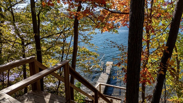 A wooden staircase leading to a dock over a body of water, surrounded by trees with autumn foliage.