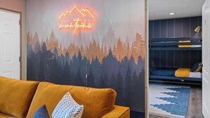 Quarto com um letreiro de neon em formato de montanha, um sofá, uma cama de beliche e um tapete estampado.