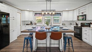 Cozinha moderna com armários brancos, uma ilha central com banquetas e uma janela ampla que oferece luz natural.