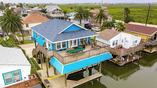Una casa frente al agua con fachada azul, un balcón y un muelle que se adentra en el agua.