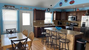 Una cocina con armarios de madera, una isla central con taburetes de bar, un refrigerador de acero inoxidable y un reloj en la pared.