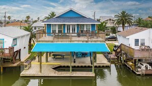 Una casa frente al mar con techo azul, un balcón y un muelle que se adentra en el agua.