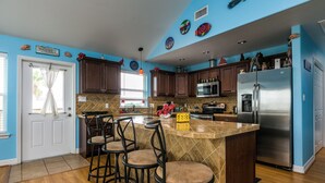 Una cocina con una isla central, taburetes de bar, armarios de madera, un refrigerador de acero inoxidable y platos decorativos en la pared.