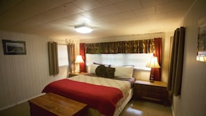 Een slaapkamer met een bed, nachtkastje, lamp, raam met gordijnen en een foto aan de muur.