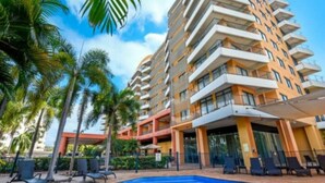 Un hotel con piscina, palmeras y un edificio de varios pisos con balcones.