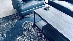 A modern living room with a blue sofa, a coffee table, and a patterned rug. - Paradise Suites Eagles Nest Apt C (Homer)