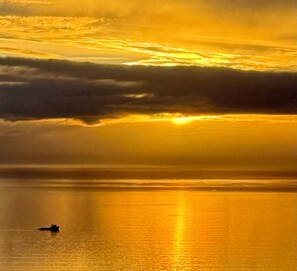 A sunset over a calm body of water with a silhouette of a boat. - Paradise Suites Eagles Nest Apt C (Homer)