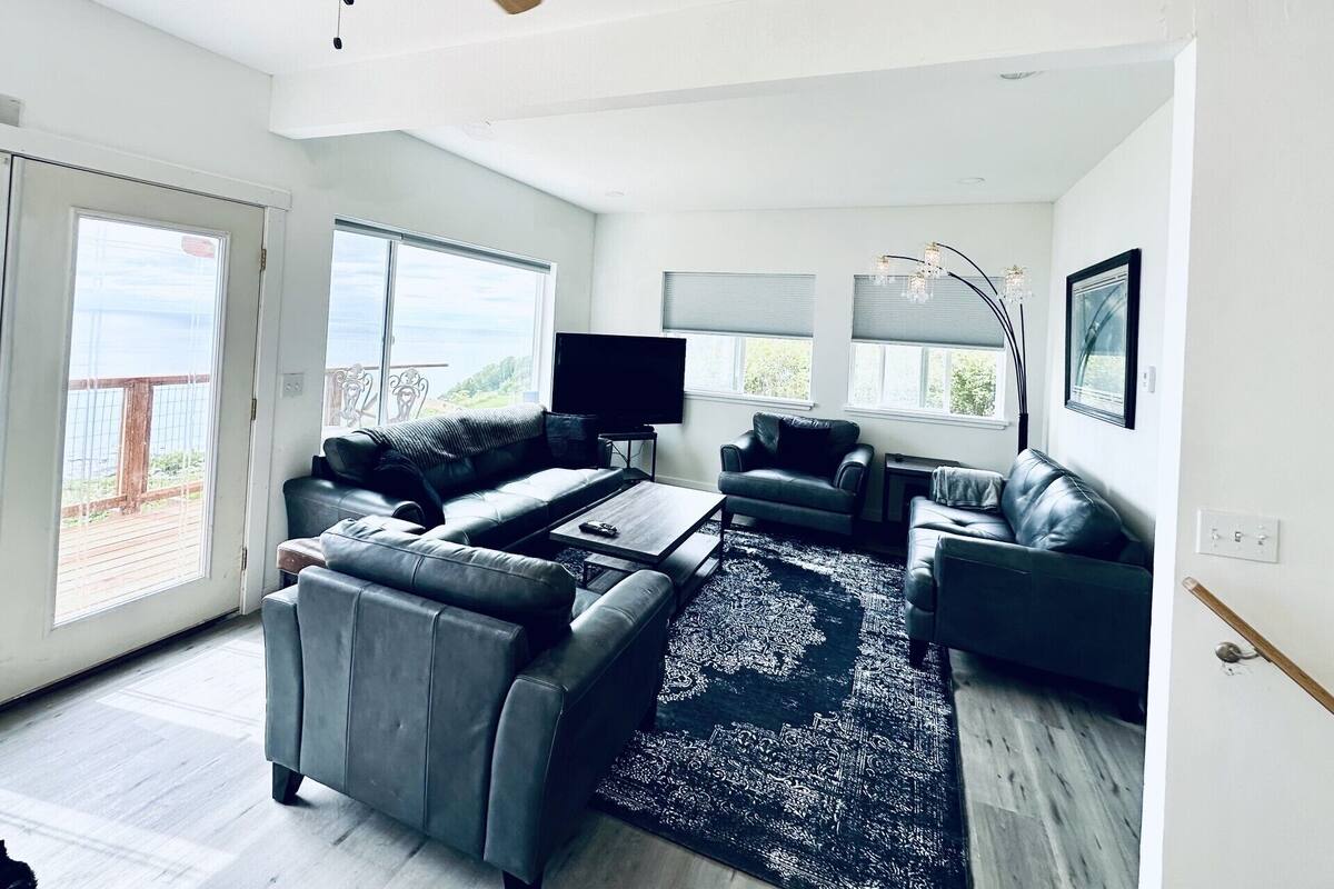 Ein geräumiges Wohnzimmer mit Deckenventilator, großen Fenstern und Blick ins Freie.