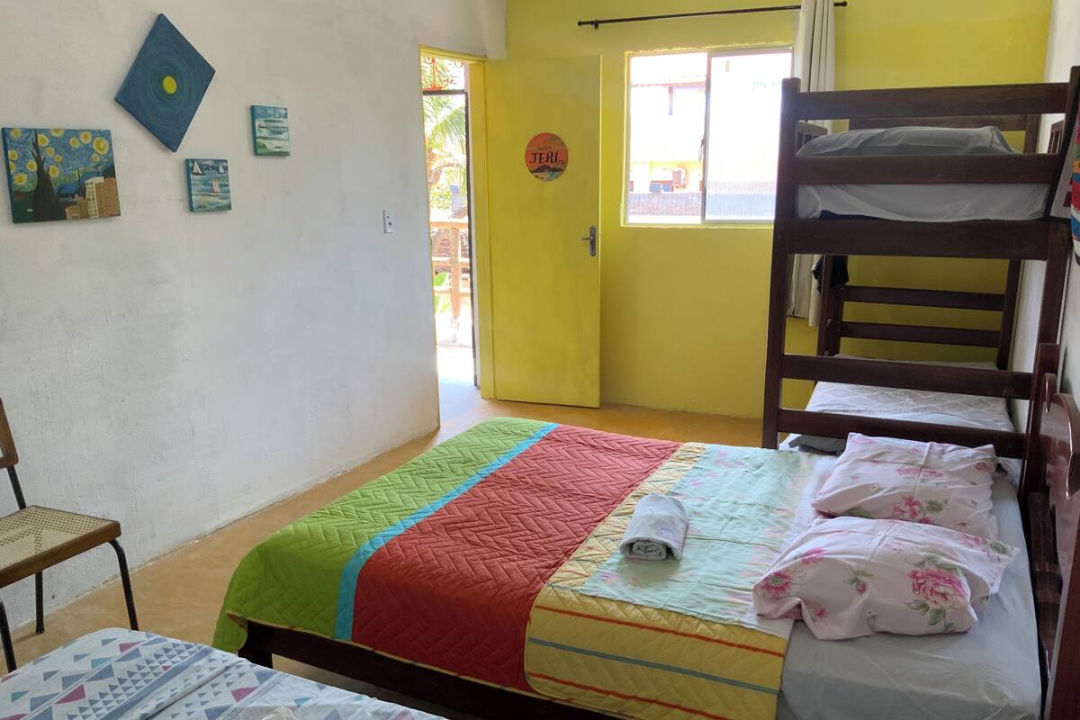 A room with a bunk bed, a single bed, a chair, and a quilted bedspread.