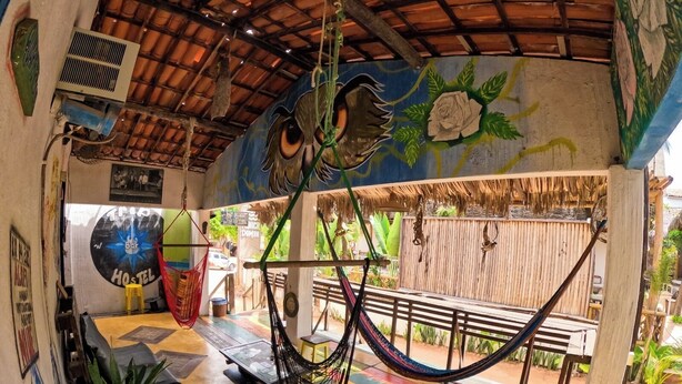 A colorful outdoor seating area with a hammock, a mural, and a thatched roof. - Trip Hostel e Pousada (Jericoacoara)