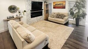 A modern living room with a large sectional sofa, a flat-screen TV, and a fireplace. - A/C, Fenced backyard , BBQ grill, pets welcome (Edmonton)