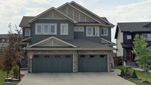 A two-story house with a garage, a stone foundation, and a well-maintained lawn. - A/C, Fenced backyard , BBQ grill, pets welcome (Edmonton)