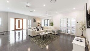 A spacious living room with a white sofa, a coffee table, and a large window with blinds.