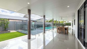 A spacious patio with a glass enclosure, a pool, and a dining area with a table and chairs.