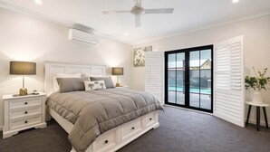 A bedroom with a bed, nightstands, a ceiling fan, an air conditioning unit, and a view of a swimming pool through the door.