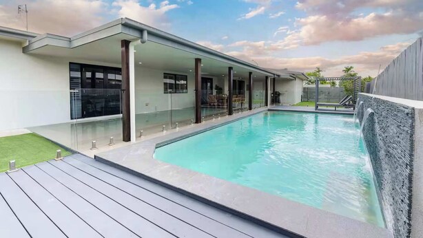 A modern pool area with a clear sky, a wooden deck, and a covered seating area.