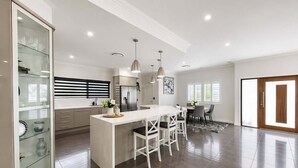 A modern kitchen with a central island, a dining area with a table and chairs, and a glass-fronted cabinet with decorative items.