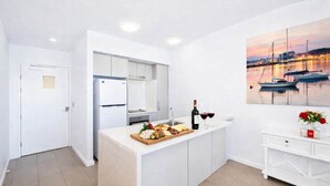 A modern kitchen with a central island, a dining area, and a view of boats on water. - Holborn 2BR Apartment with Pool, Gym & Parking in Townsville CBD (Townsville City)