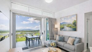 A modern living room with a dining area, a sofa, and a painting of a landscape. - Holborn 2BR Apartment with Pool, Gym & Parking in Townsville CBD (Townsville City)