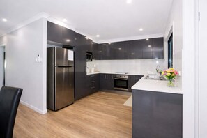 A modern kitchen with dark cabinets, stainless appliances, and a wooden floor.