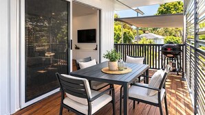 Una terraza con mesa y sillas, una parrilla y un televisor al fondo.