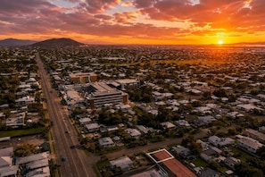 Vista aérea de una zona residencial con una calle principal, un complejo de edificios grande y un atardecer en el fondo.