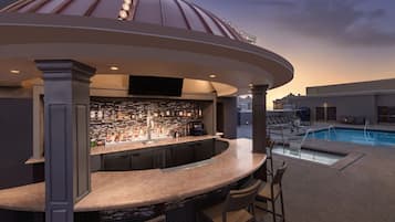 Een bar met uitzicht op het zwembad, met een gebogen bar, diverse zitplaatsen en een goed gevulde bar.