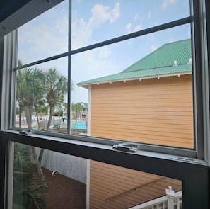 Guests can enjoy a view of the surrounding landscape from the room's window, featuring a building with a green roof and palm trees.