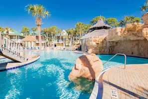 Relax by the resort pool surrounded by palm trees and a thatched-roof structure.