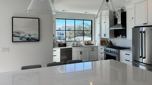A modern kitchen with white cabinets, a large island, stainless steel appliances, and pendant lighting. - The Lookout | Private Pool | Steps to Beach & Pier | Newly Built (Folly Beach)