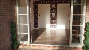 A spacious entrance with a wooden floor, two white doors, and a floral wallpaper.