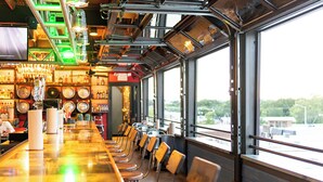 Un bar doté d’un long comptoir, de nombreux tabourets et offrant une vue sur l’extérieur grâce à de grandes fenêtres.