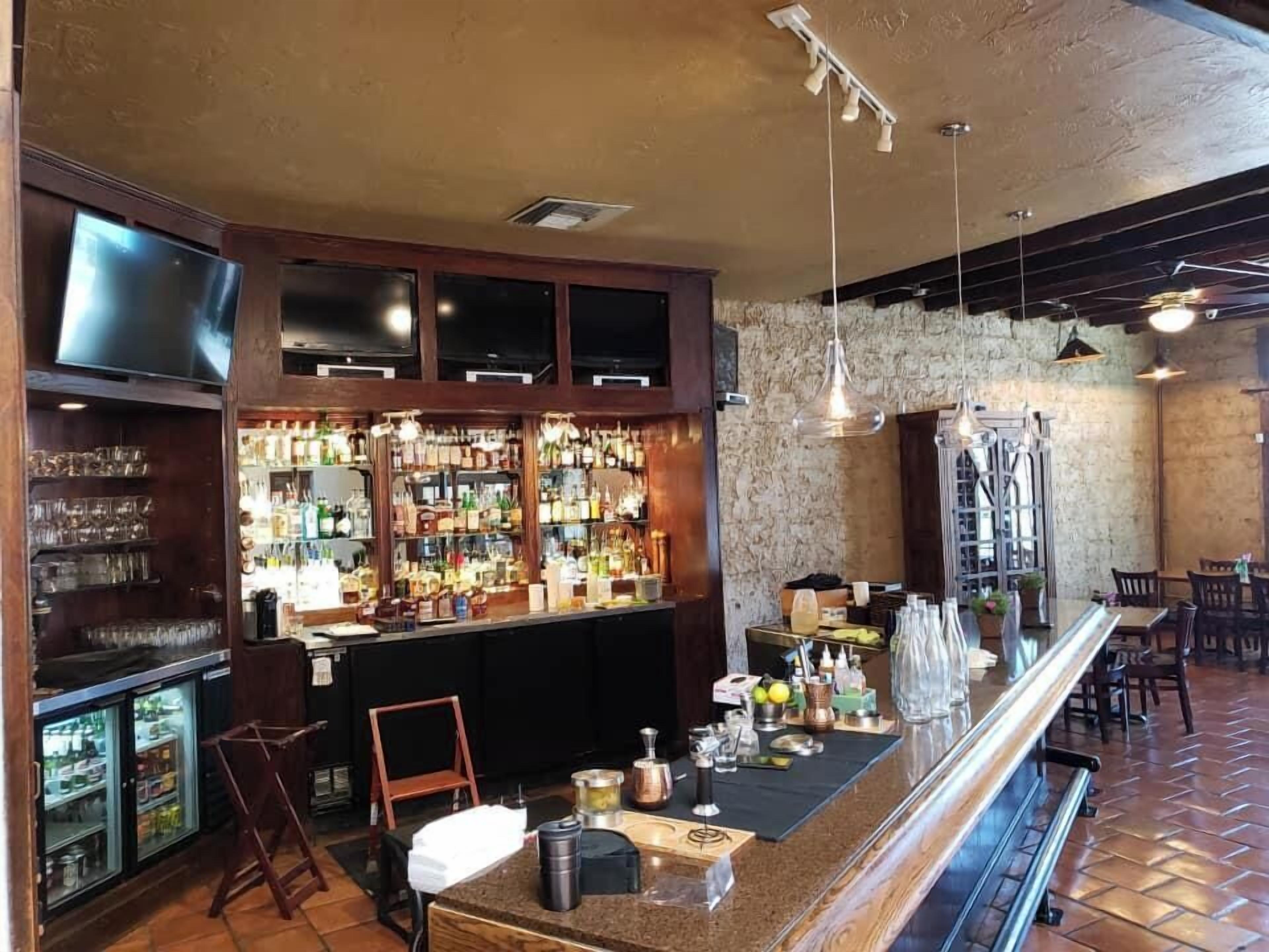 Una zona de bar con una barra larga, estantes con botellas y un televisor montado en la pared.