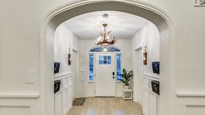 Un couloir aux murs blancs, avec un plancher en bois, une porte blanche et un lustre. De chaque côté, on trouve des boîtes aux lettres numérotées.
