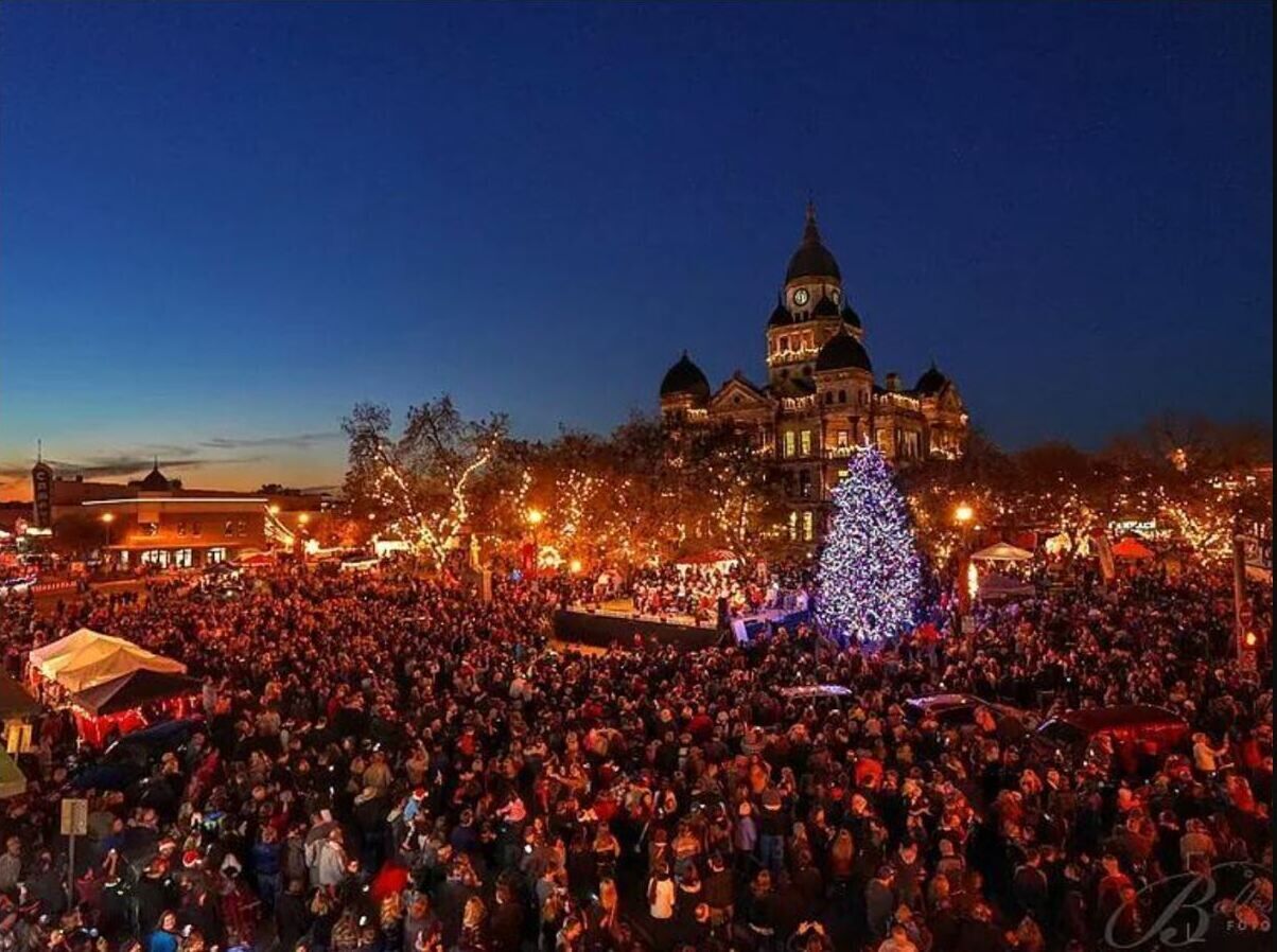 A large crowd gathered in an outdoor area with a prominent building featuring domed architecture in the background.