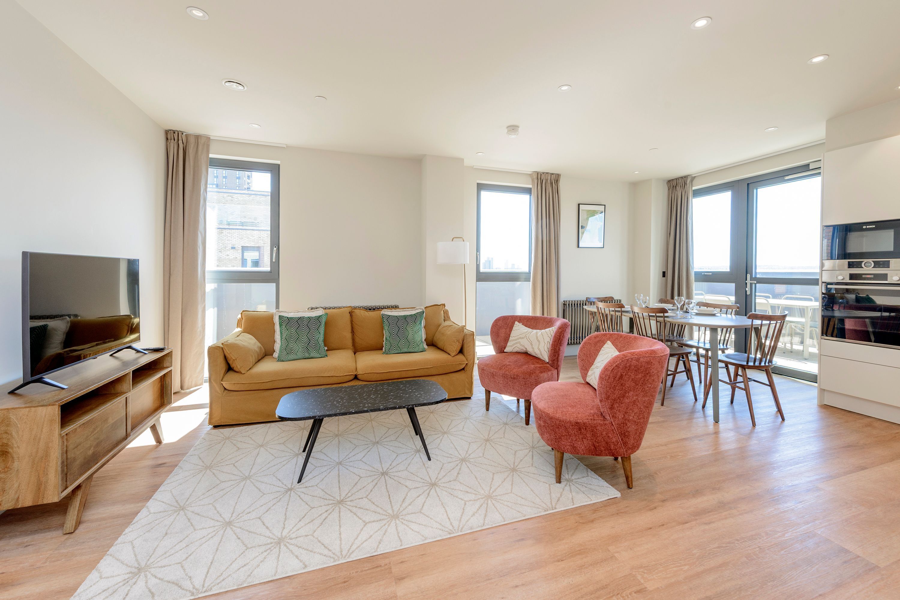 Una sala de estar moderna con un sofá, sillones, una mesa de centro y un televisor. Hay un comedor con sillas y una mesa.