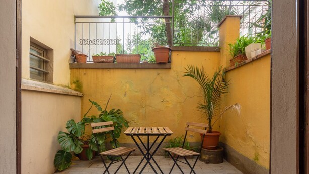 A small outdoor patio with a wooden table and two chairs, surrounded by potted plants and a yellow wall. - One-bedroom apartment with Patio n.2 (Firenze)