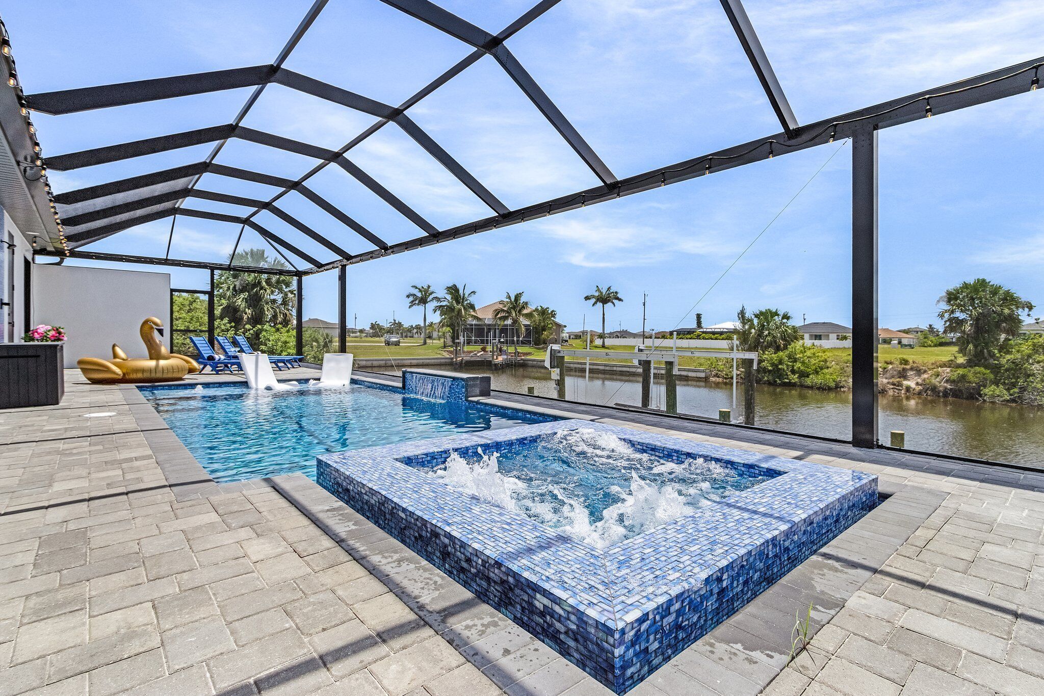 A covered outdoor swimming pool with a hot tub, lounge chairs, and a view of a lake.