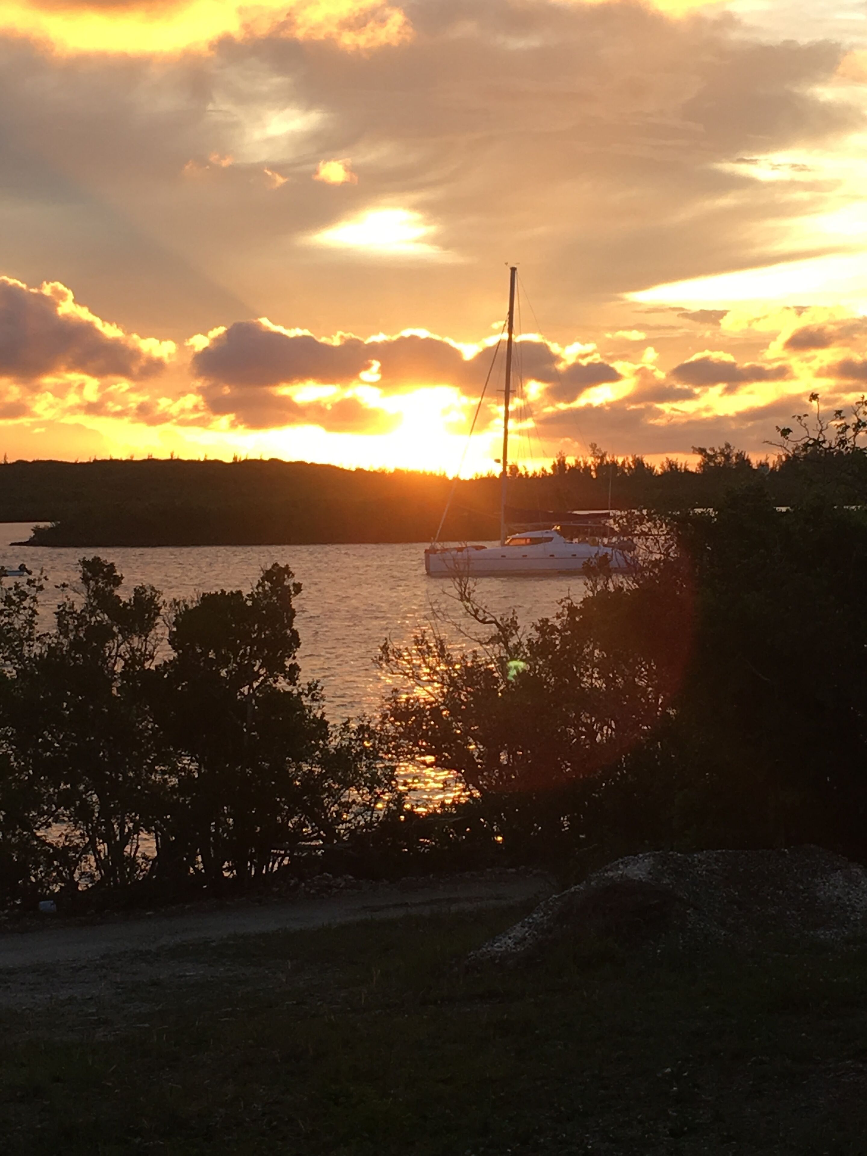 A sunset over a body of water with a sailboat anchored near the shore.