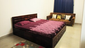 A bedroom with a bed, a brown sofa, and a window with blue curtains.