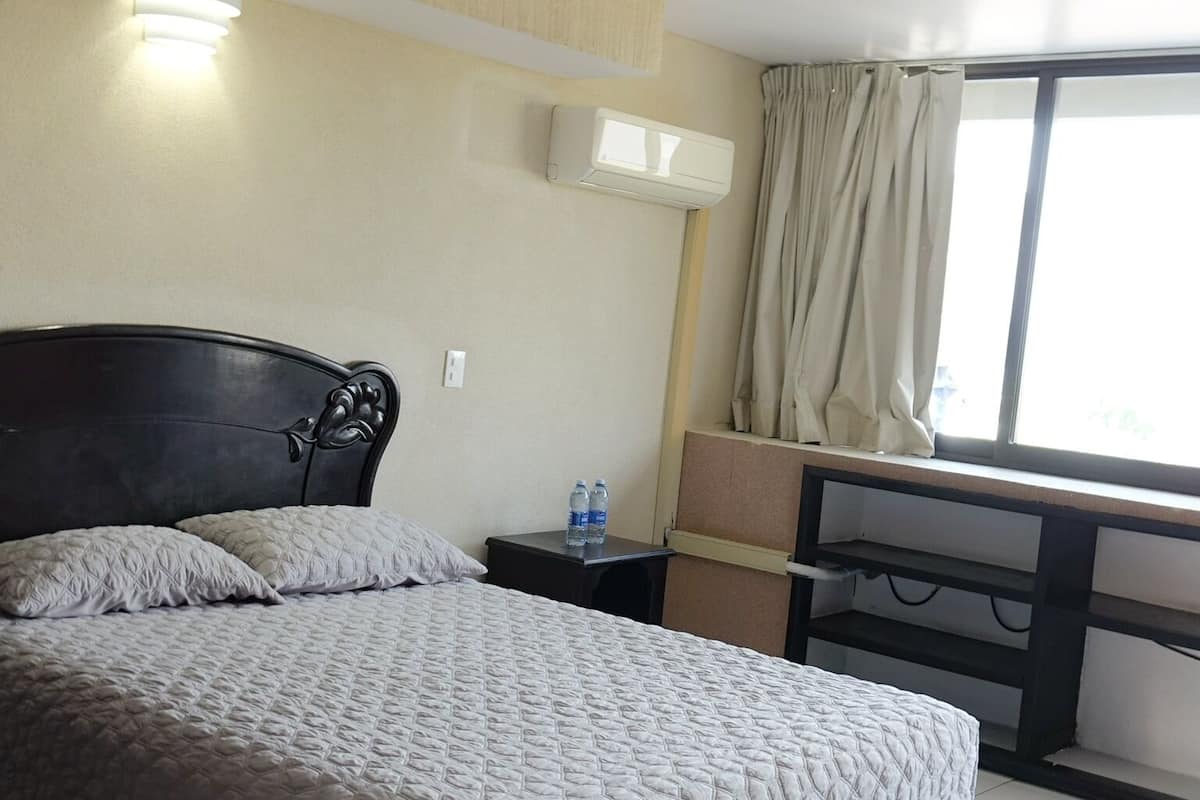 Ein Hotelzimmer mit Bett, Nachttisch, Klimaanlage und einem Vorhangfenster.